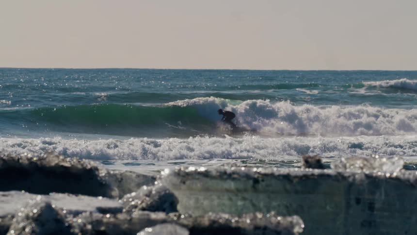 A man surfing waves near a coast covered in ice