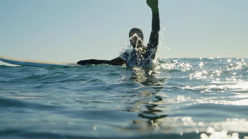 A surfer raises his arm up high in the ocean