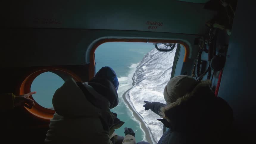 Two men point out of the plane window towards the shore