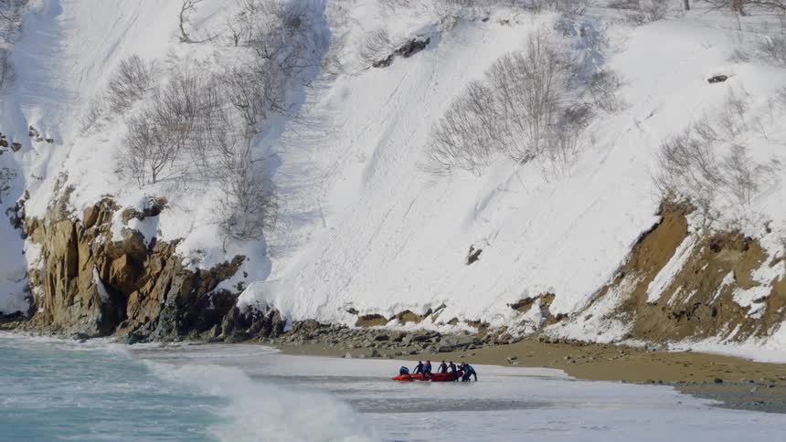 A small orange boat arriving at a shore and people get off it to push it onto the sand