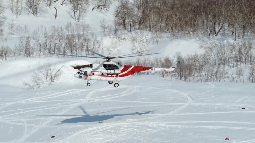 A red and white helicopter taking off from a snowy field