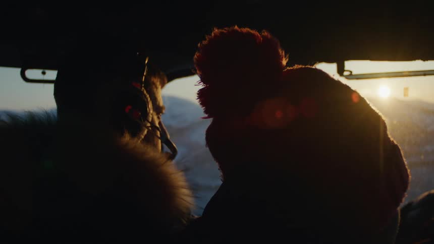 The heads of two people who are back to back and wearing hats and looking at a place with sunlight on the horizon
