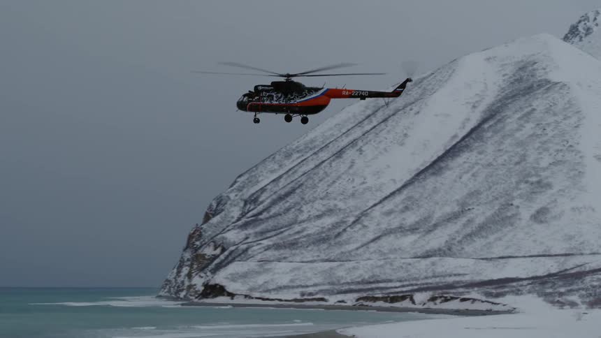 A helicopter flying low over a snowy landscape with a mountain in the background
