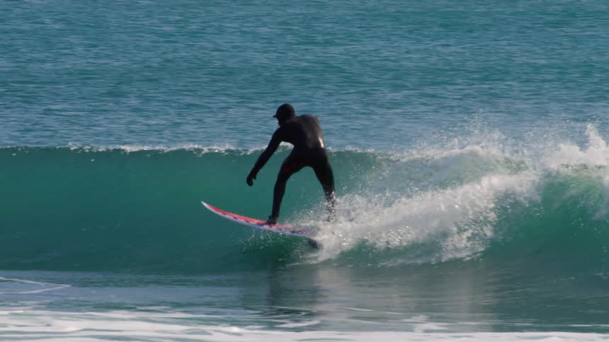 Surfer wearing a wetsuit rides a wave on a sunny day