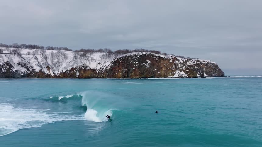 Aerial view of a person riding a big wave and surfing