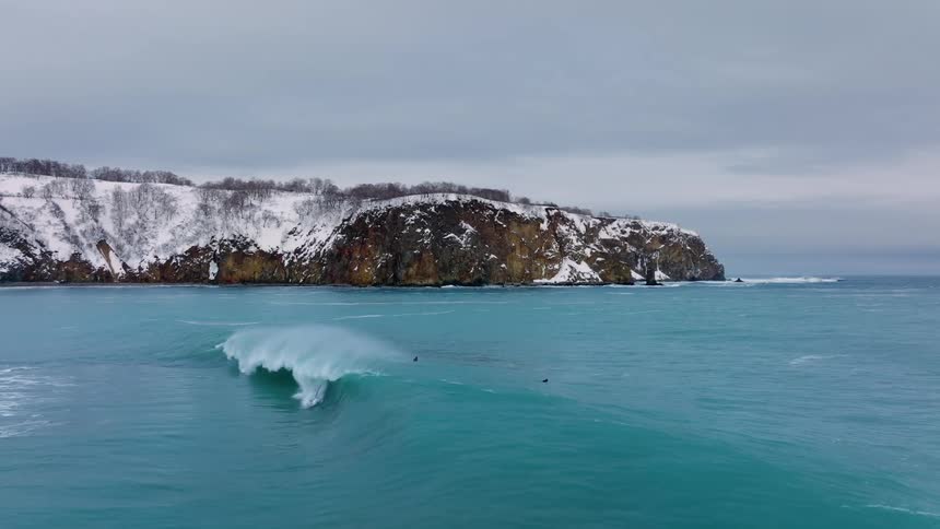 Aerial view of a surfer riding a wave and falling into the sea after making a mistake