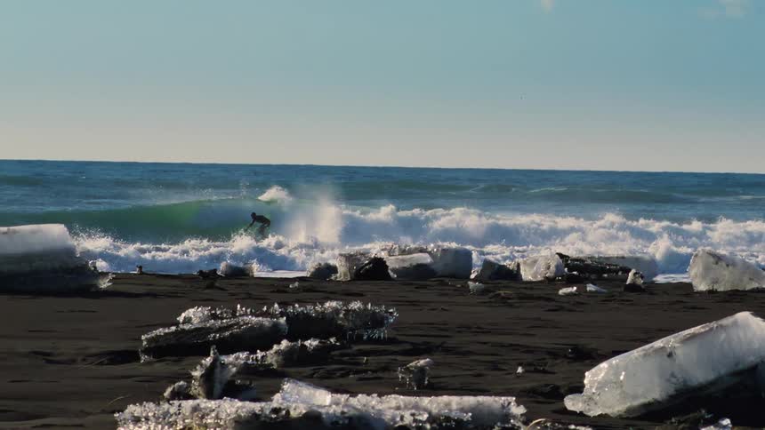 A surfer rides an ocean wave near an icy coast on a sunny day
