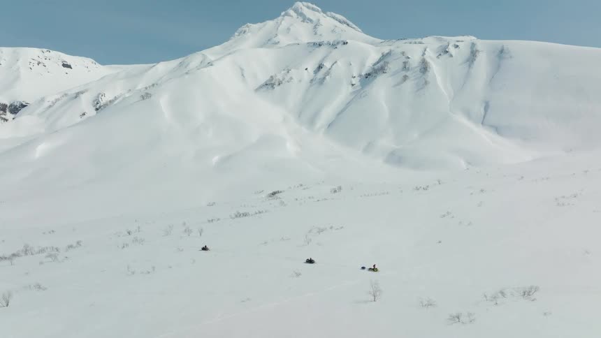 Three snowmobiles traverse a vast snowy landscape with a backdrop of rugged snowcovered mountains