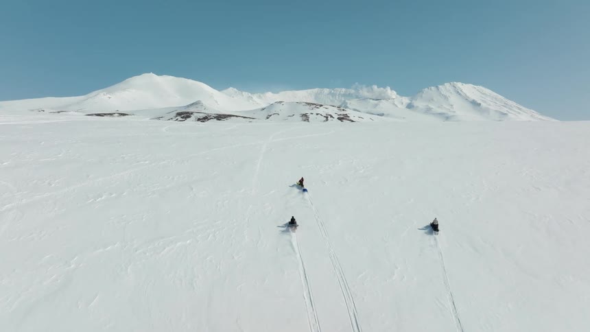 Aerial view of three people on snowmobiles climbing a mountain