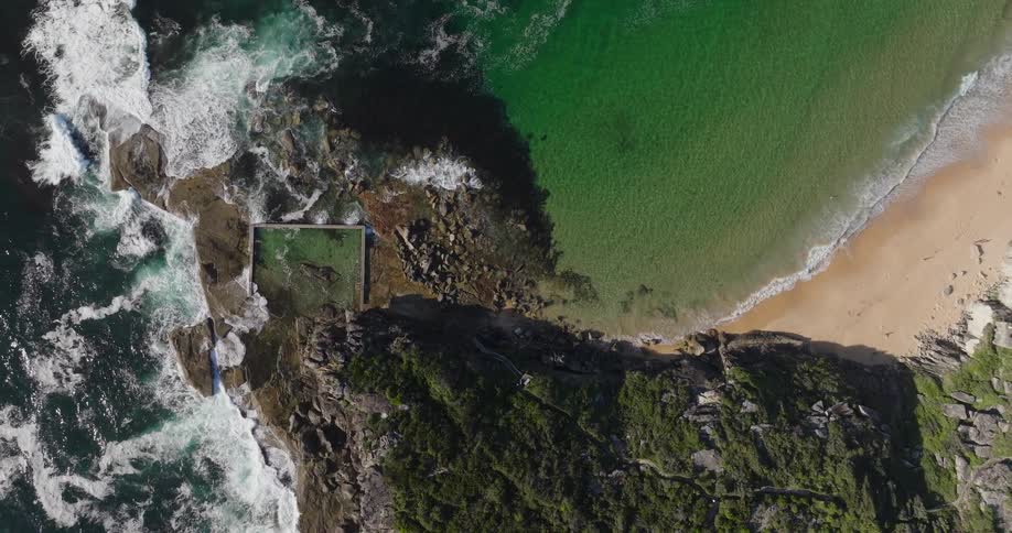 An aerial view of a coastal scene with a vibrant green pool nestled into the rocky shoreline