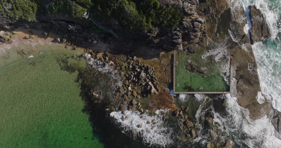 An aerial view of a rocky coastline features a natural rock pool filled with water