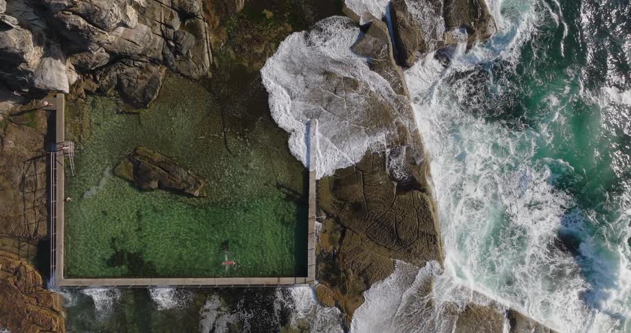 Aerial view of people swimming in a natural pool on a rock surrounded by the sea