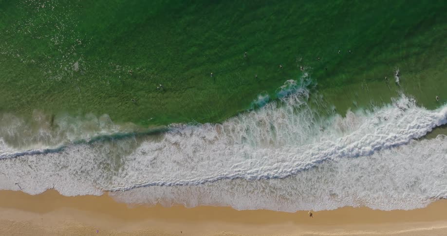 An aerial view of a beach with waves crashing on the shore and people surfing in the water