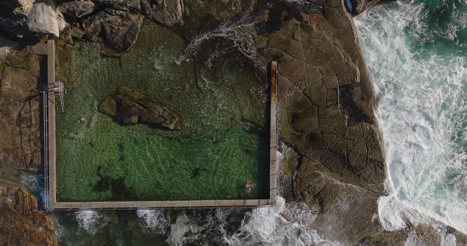 Aerial view of a natural pool with people next to the sea