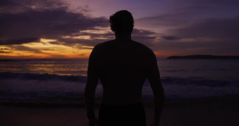 Silhouette of a man with his back facing the sea with the purple and orange sky