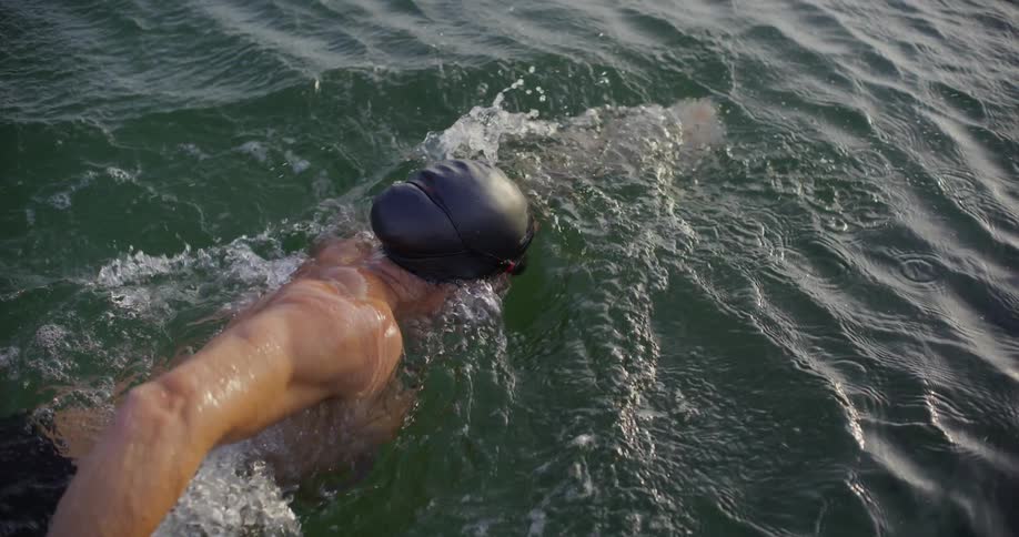 Male is swimming in a body of water in slow motion