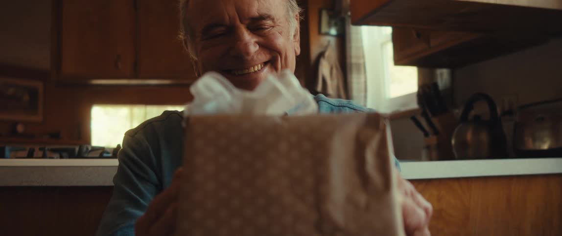 Elderly man smiles warmly as he holds a gift wrapped with decorated paper and a ribbon