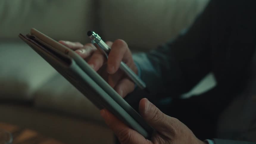 A hand poised with a stylus gestures over a tablet device