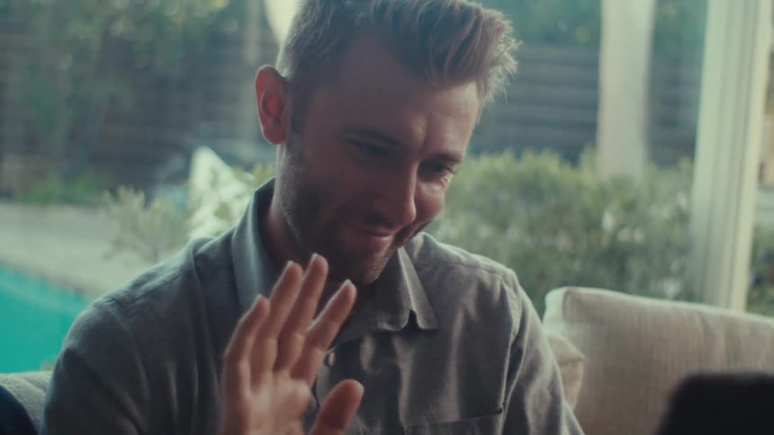 Man sitting down making a hello sign in front of a tablet