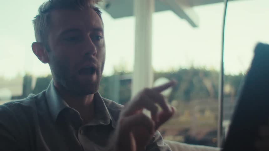 A person is talking on a smartphone in a bright indoor space with large windows overlooking greenery