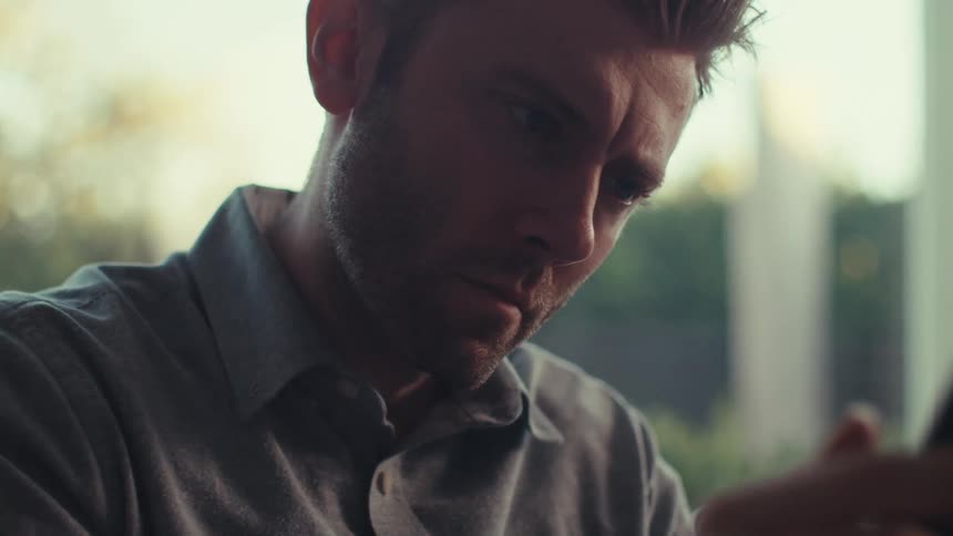 A man is sitting indoors and texting on his cellphone