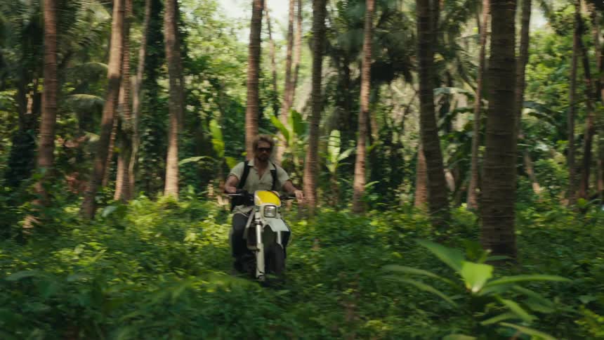 In a tropical forest a man is driving a scooter