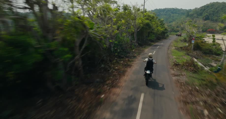 Aerial view of a person riding a motorcycle on a road through the countryside