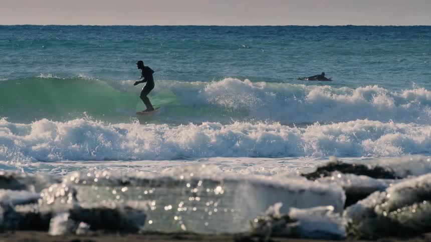 A man surfs the waves near an icecovered coast
