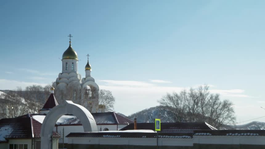 A snowy winter day in russia features a white russian orthodox church with prominent gold domes behind an arched gate
