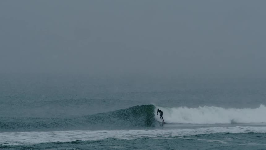 A surfer rides a wave under a light snowstorm