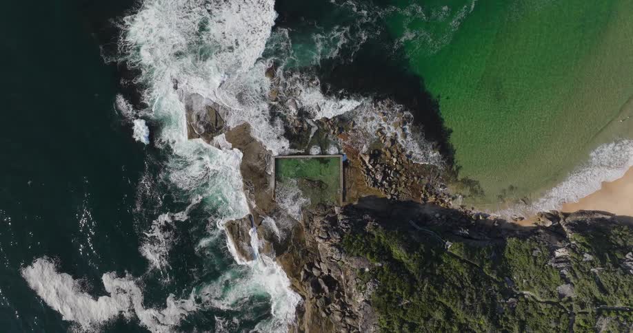 Aerial view of a rocky coastline where waves break violently against the rocks creating white foam