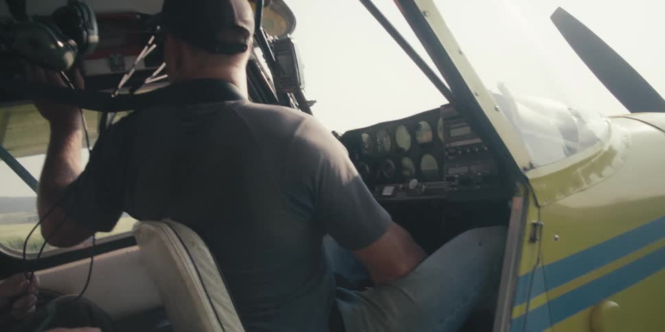 A person is seated in the cockpit of a small aircraft adjusting the controls