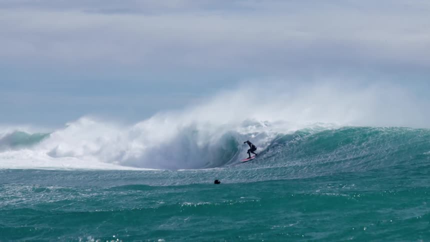 Surfer surfing large wave as other surfer paddles by