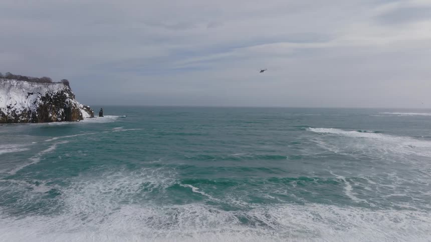 Aerial panorama of a helicopter flying over the sea with the rocky snowy coast in the background