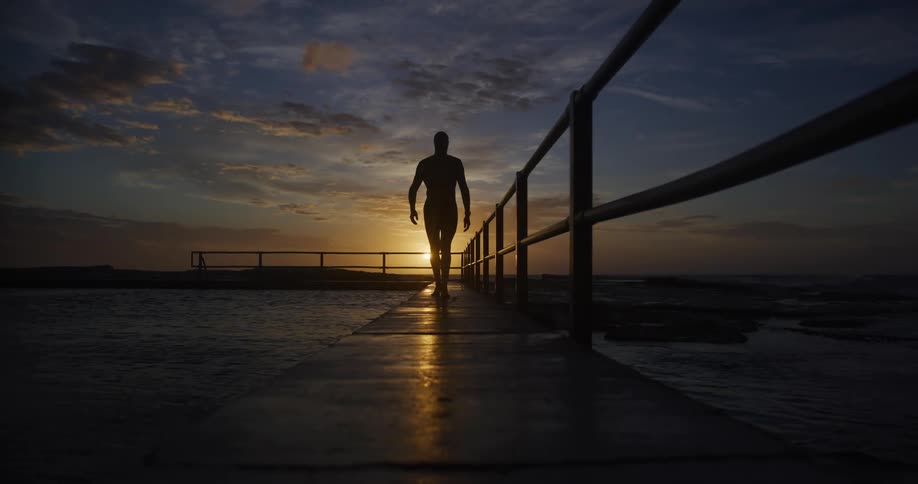 Male walking on a pathway over a body of water at dusk