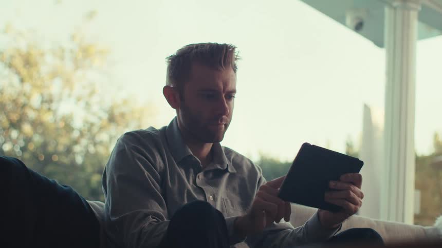 A man is shaking his head as he swipes on his tablet