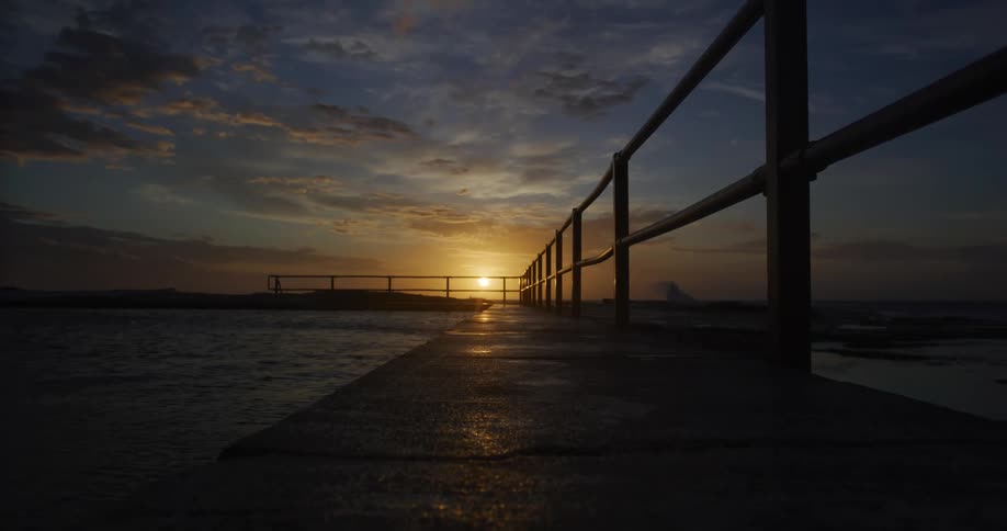 The sun sits on the horizon with a pier in the foreground
