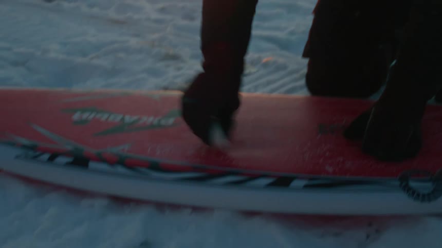 A man is polishing his surfboard on the beach