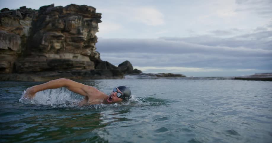 A man is swimming past the cliff