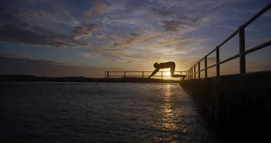 Silhouette of a person jumping into a water tank while swimming
