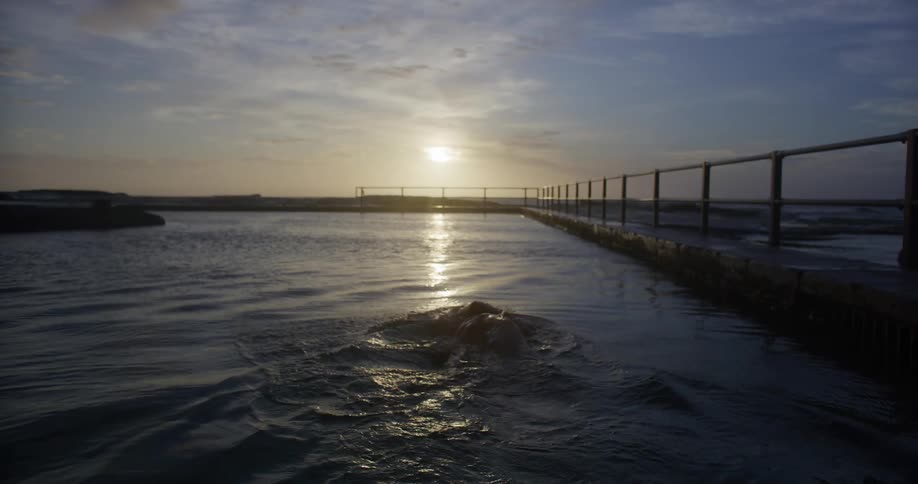 Person swimming in a canal with the sea and the sun in the background