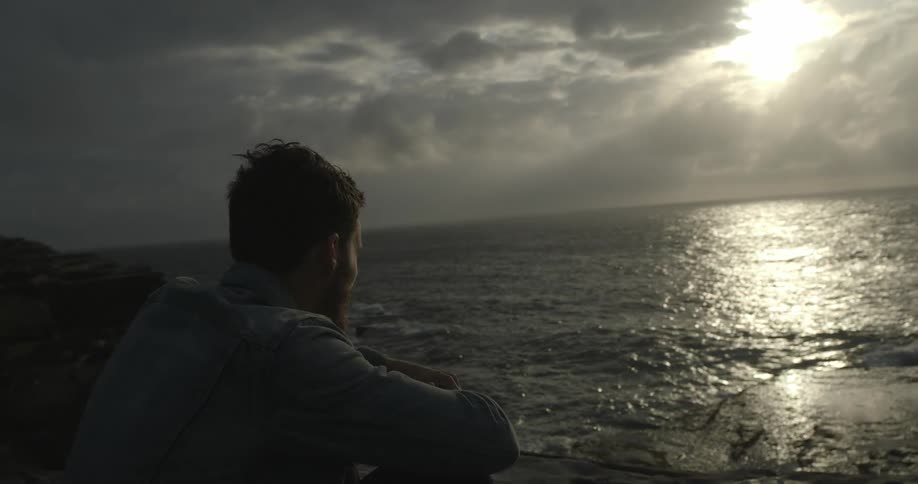 Man sits and watches the shore on a cloudy day
