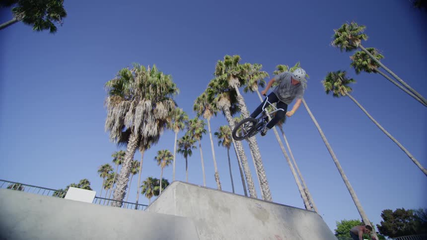 Man does a bike jump off a ramp with tall palm trees ahead