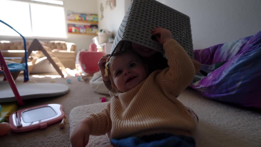 Girls play with a plastic basket in a playroom at home