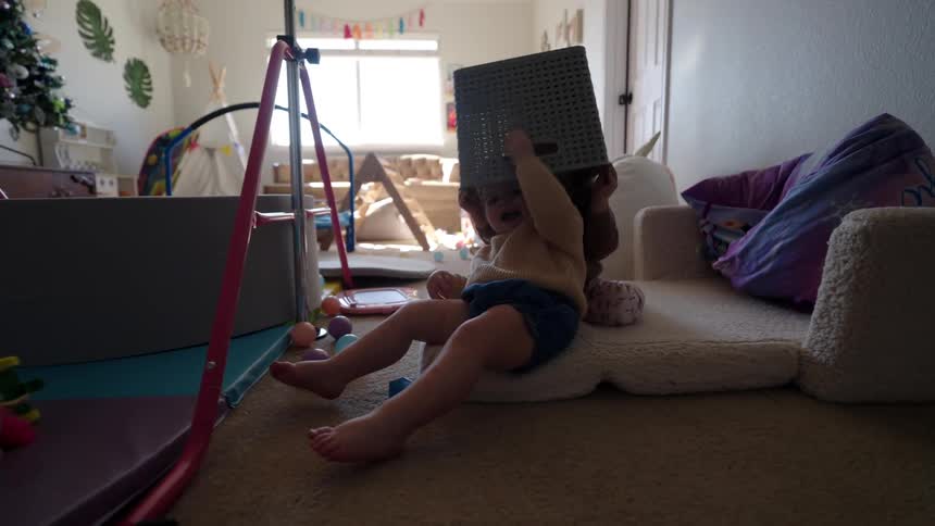 Two small children playing in a room with a basket of clothes on their heads