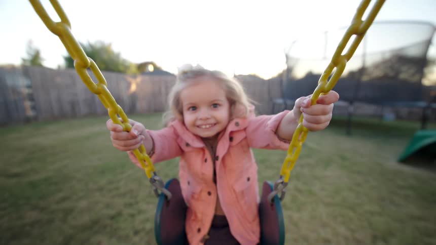 Little blonde girl having fun on a swing in a backyard