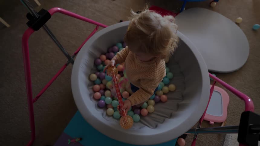 A girl plays with a colorful lightup wand while standing in a small ball pit in her bedroom