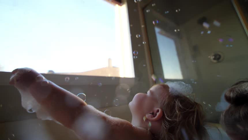 Two small children taking a bath in a bathtub with foam and soap bubbles
