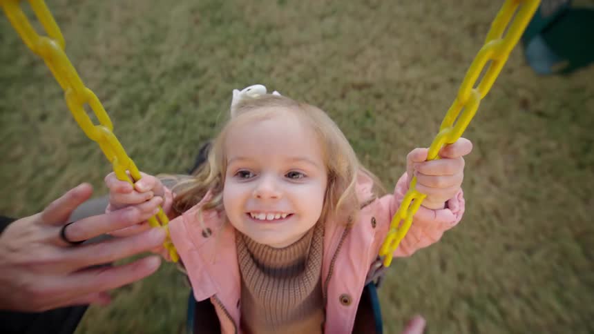 A parent is pushing his daughter on a swing