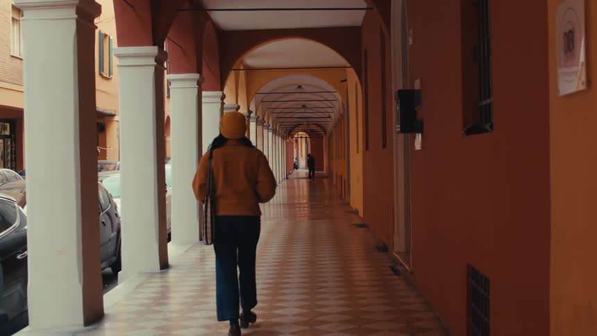 Pedestrian walking in an open corridor next to the street with parked cars